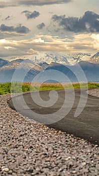 Vertical Curving road with view of lake snow capped mountain and cloudy sky at sunset