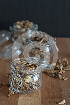 Vertical dark photo of sliced, chopped and dried various mushrooms in three preserving glass bowls standing on wooden seat or