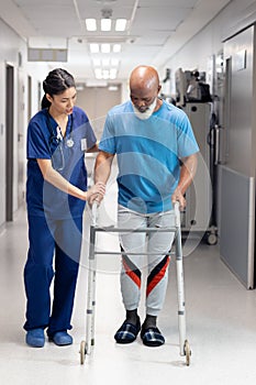 Vertical of diverse female doctor helping senior male patient use walking frame, copy space