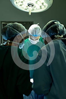 Vertical of diverse group of surgeons operating on patient in operating theatre, with copy space