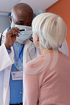 Vertical of diverse senior male doctor examining eye of female patient with penlight, copy space
