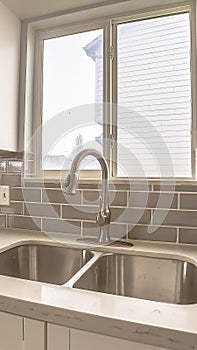 Vertical Double bowl stainless steel sink against tiled wall with window and cabinets