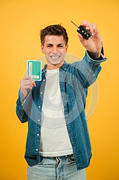 Vertical excited Young Man Holding Car Keys and New Driver L Sign Against a Vibrant Yellow Background. Caucasian guy