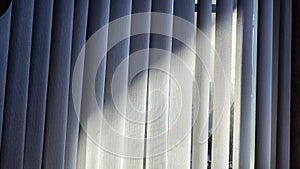 Vertical fabric white blinds on the window with light and shadow from the sun. Background and texture. Abstract pattern