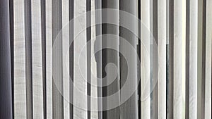 Vertical fabric white blinds on the window with the sun. Background and texture. Abstract pattern and frame. Stripes and