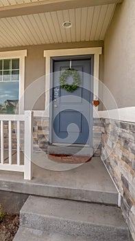 Vertical Facade of a home with railing on the porch and front door decorated with wreath