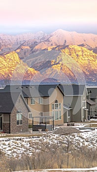 Vertical Facade of homes with snowy sunlit mountain and calm lake background at sunset