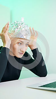 Vertical. Fearful young woman with aluminum hat browsing social media. Conspiracy theory about 5g microwaves