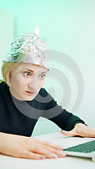 Vertical. Fearful young woman with aluminum hat browsing social media. Conspiracy theory about 5g microwaves