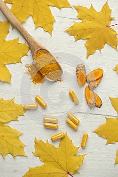 Vertical flat background with yellow leaves and turmeric in different shapes Capsule and powder in a wooden spoon and root cut