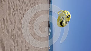 Vertical format video of summer beach with yellow parasailing wing flying in wind