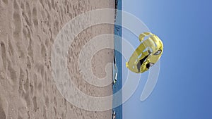 Vertical format video of summer beach with yellow parasailing wing flying in wind