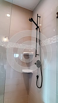 Vertical frame Black round shower head on tile wall of shower stall with hinged glass door