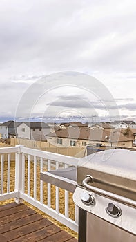 Vertical frame Brown wooden deck with white railing overlooking yard homes and cloudy sky