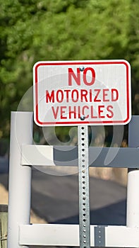 Vertical frame Close up view of a No Motorized Vehicle sign against a road with a white gate