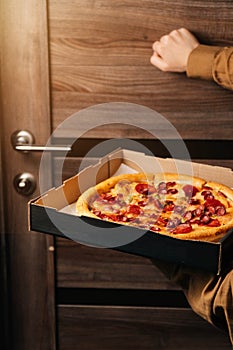 A vertical frame of the girl holds a pizza and knocks on the door. the concept of food delivery