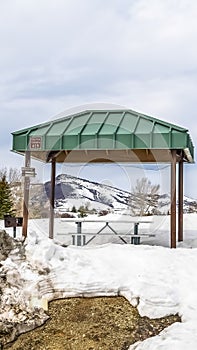 Vertical frame Green cabana with barbecue grill and picnic table at a snow covered park