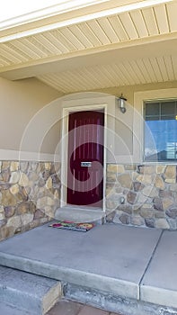 Vertical frame Home facade with maroon front door and combination of concrete and stone wall