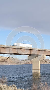 Vertical frame Huge trucks travelling on a massive bridge against snowy hills and cloudy sky