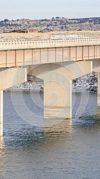 Vertical frame Massive bridge over shiny lake with grassy and snowy landscape background