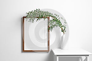 Vertical frame mockup for artwork on white wall with natural eucalyptus twigs