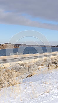 Vertical frame Snow covered terrain along a road overlooking mountain and lake in winter