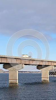 Vertical frame Truck travelling on a beam bridge over lake against rugged land and cloudy sky