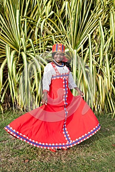 The vertical full body of a joyful African American woman in a bright colorful national Russian dress