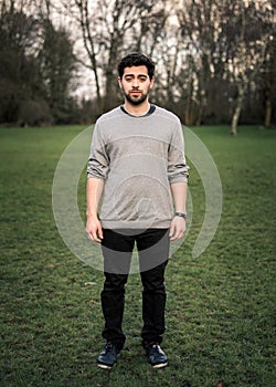 Vertical full body photo of a young man standing isolated in a park, looking at the camera