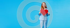 Vertical full-length portrait redhead elegant woman in cute pyjama, holding big red heart sign, valentines day gift and
