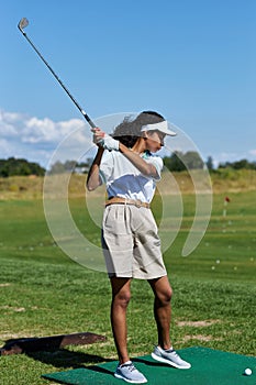 Vertical woman playing golf on green grass and swinging golf club