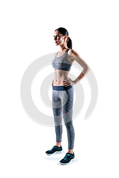 Vertical full-size full-length half-turned portrait of slim sportive beautiful young attractive sport woman, she is staying