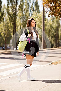 Vertical full size photo of lovely cute girl wear uniform skirt long socks bag on shoulder go to school on green city