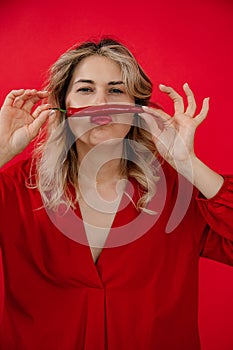 Vertical funny, creative blonde woman in red outfit holding red hot pepper in hands under nose like mustache. Hot news
