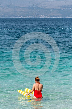 Vertical of a girl in a red swimsuit entering the beautiful turquoise sea with a swimming ring