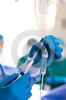 Vertical of gloved hand of surgical tech preparing iv bag in operating theatre, with copy space