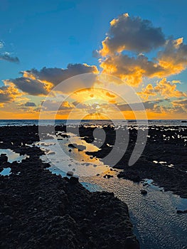 Vertical of the glowing sun hiding behind the fluffy clouds at sunrise over the beach