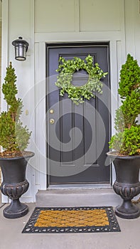 Vertical Gray front door of a home with green wreath and flanked by tall potted plants