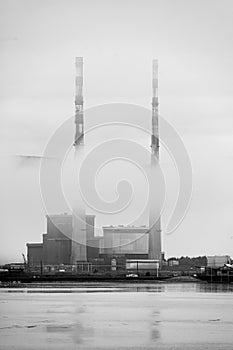Vertical grayscale shot of industrial towers in misty weather