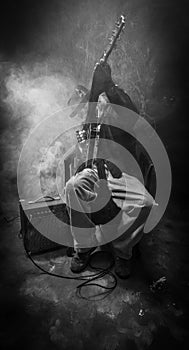 Vertical grayscale shot of an old guitarist sitting in the dark corner with smoke