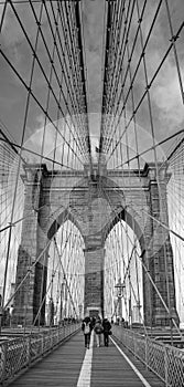 Vertical grayscale shot of people walking on Brooklyn Bridge in NYC, USA