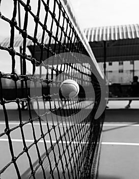 Vertical grayscale shot of a tennis ball hitting a net