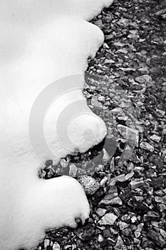 Vertical greyscale of the ground covered in small rocks and snow in winter