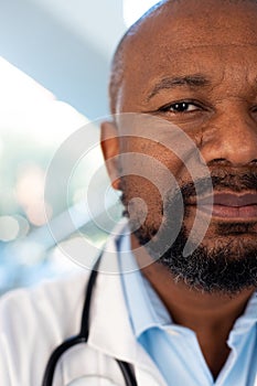 Vertical half face portrait of smiling african american male doctor in hospital corridor photo