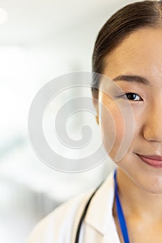 Vertical half face portrait of smiling asian female doctor in hospital corridor, with copy space photo