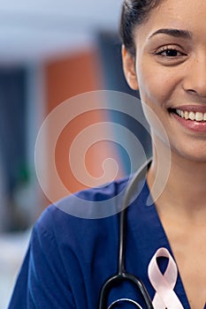 Vertical half face portrait of smiling biracial female doctor wearing cancer ribbon, copy space