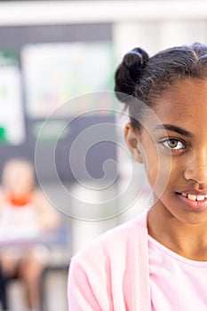 Vertical half face portrait of smiling biracial schoolgirl in classroom with copy space photo