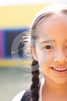 Vertical half face portrait of smiling cauasian elementary schoolgirl in schoolyard, copy space photo