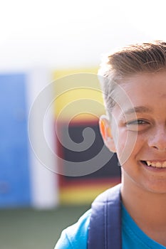 Vertical half face portrait of smiling caucasian elementary schoolboy in schoolyard, copy space photo