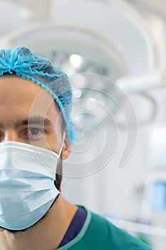 Vertical half portrait of caucasian male surgeon in surgical mask and cap in operating theatre